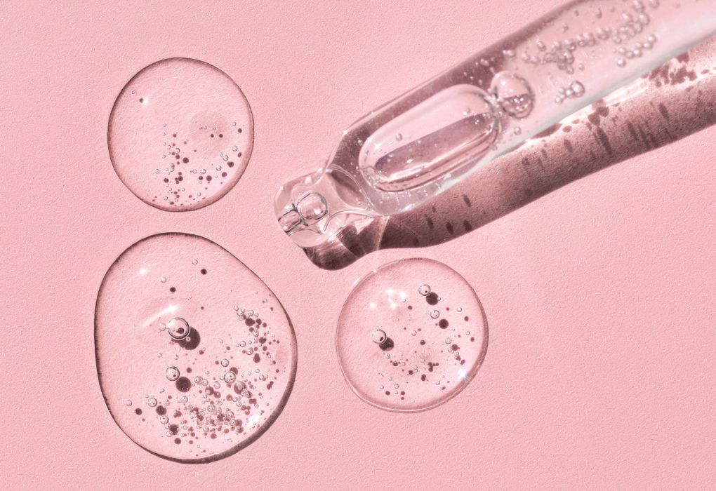 Pipette mit Hyaluronserum und klaren Tropfen auf rosa Hintergrund