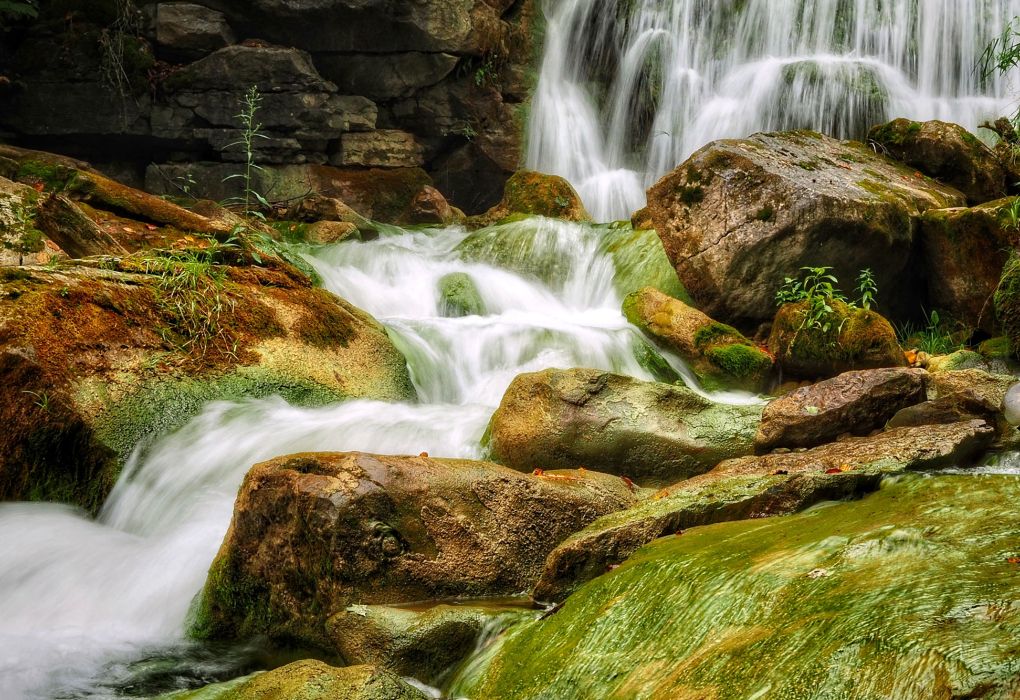 Wasserfall fließt über moosbewachsene Felsen in einem grünen Wald