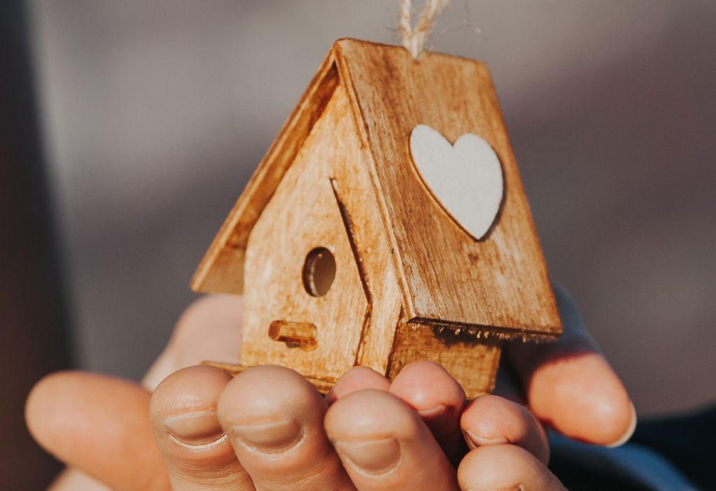 Hände halten ein kleines Holzhaus mit ausgestanztem Herz in der Mitte