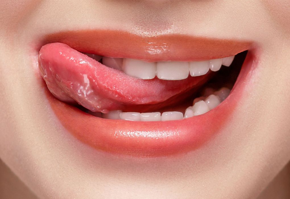 Frau lächelt und fährt mit der Zunge spielerisch über ihre weißen Zähne