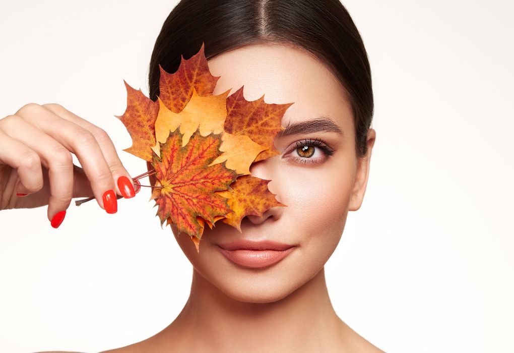 Frau mit Herbstblättern vor dem Gesicht, Symbol Hautpflege