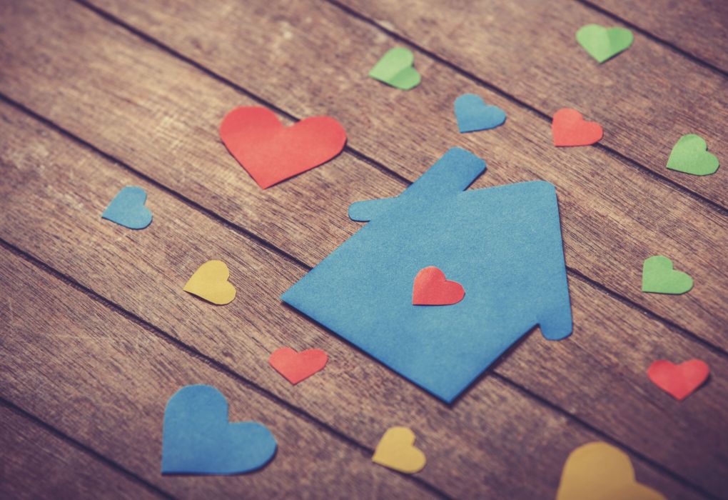 Bunte Papierherzen und ein blaues Papierhaus auf Holzboden