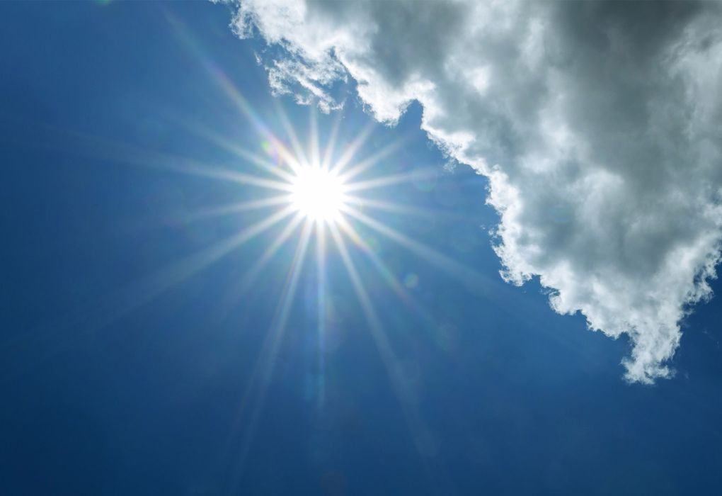 Starke Sonnenstrahlen brechen durch weiße Wolken am blauen Himmel