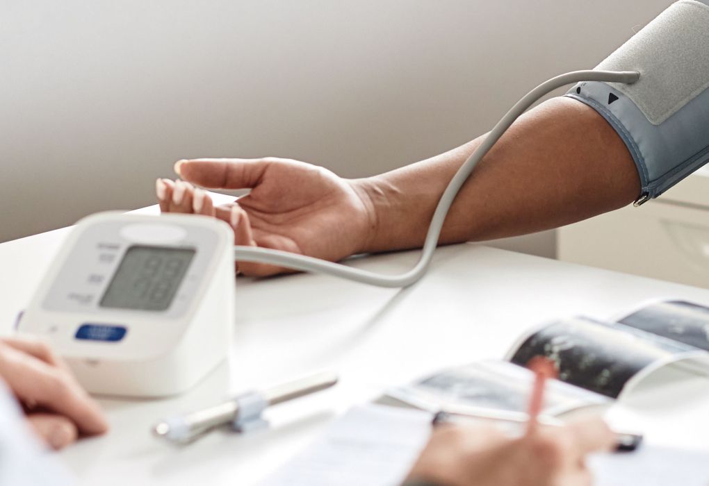 Person misst den Blutdruck mit elektronischem Messgerät am Arm in einer Praxis