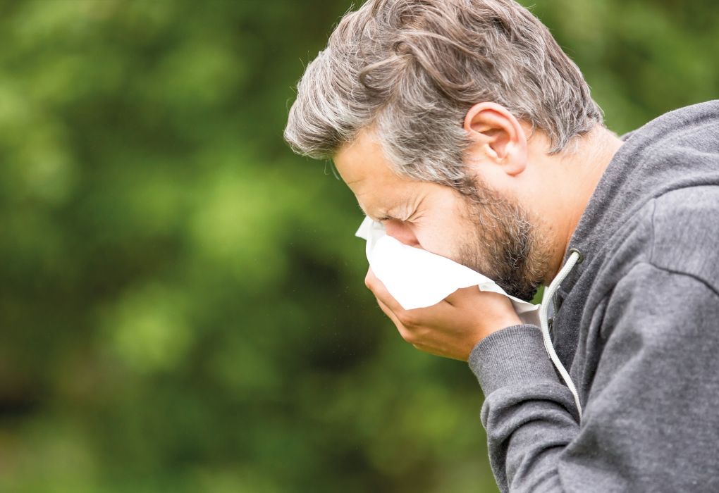 Mann niest in ein Taschentuch im Freien