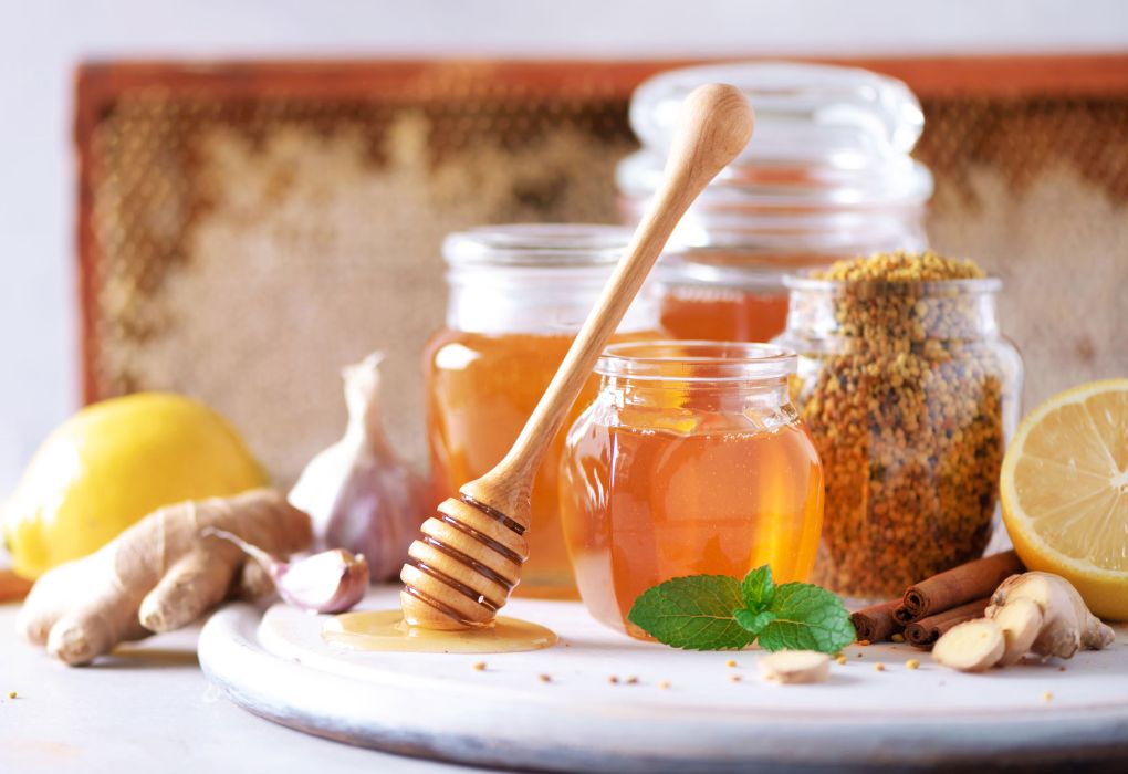 Glas Honig mit Holzlöffel, Zitrone und Ingwer auf einem Teller als traditionelles Hausmittel
