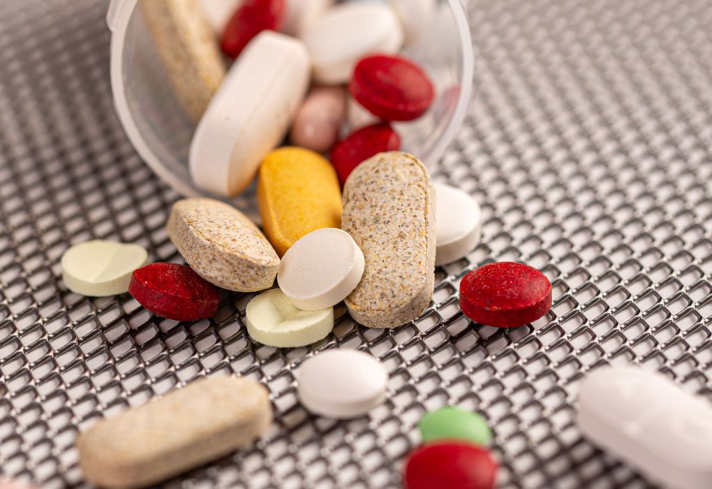 Verschiedene Vitamin-Kapseln und Tabletten in bunten Farben auf grauer Unterlage