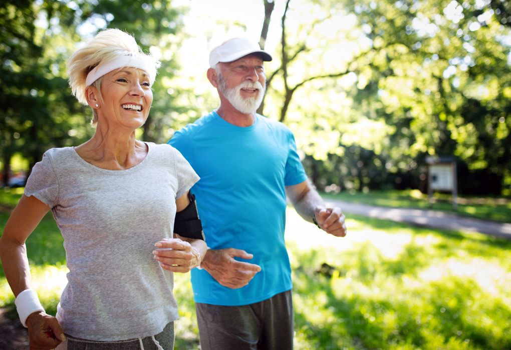 Älteres Paar joggt lachend bei Sonnenschein im Park
