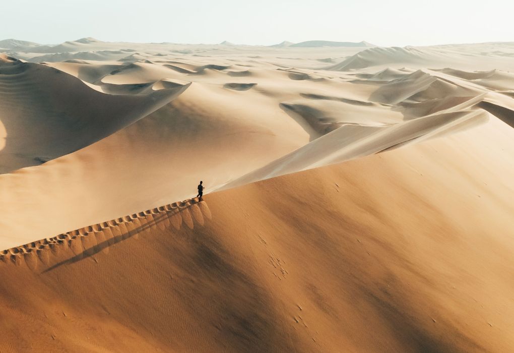 Goldfarbene Sanddünen mit winziger Menschenspur in weiter Wüstenlandschaft