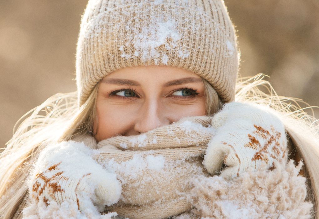 Frau mit Strickmütze und Schal bedeckt Mund und Nase bei kaltem Wetter.