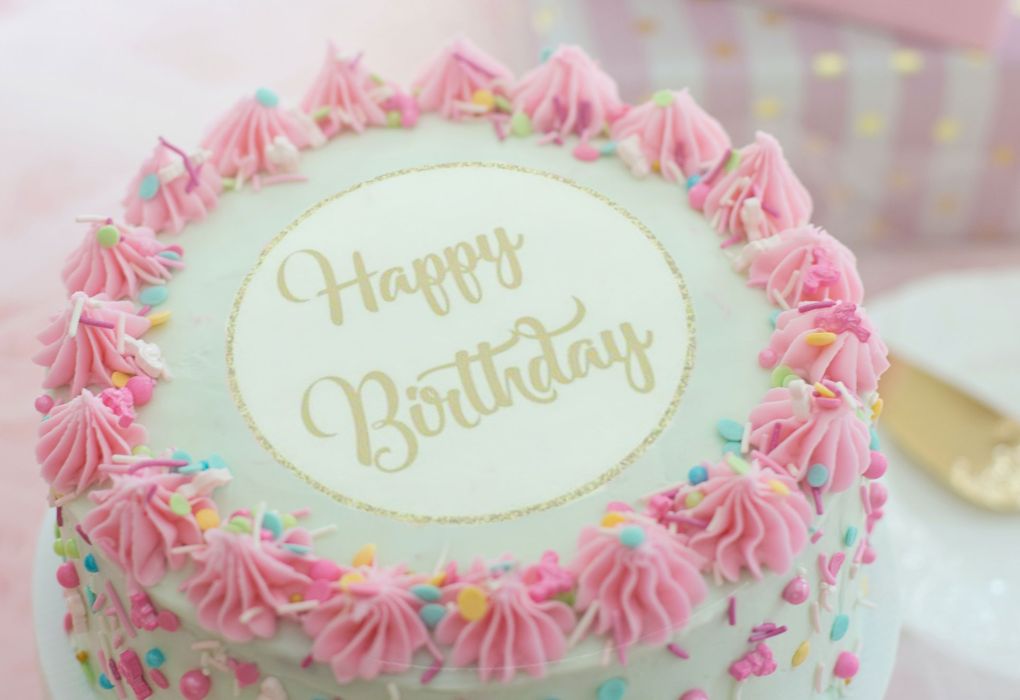 Rosa verzierte Torte mit Aufschrift „Happy Birthday“ und Blumen-Deko.