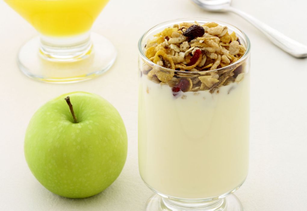 Glas mit cremigem Joghurt und Topping, daneben grüner Apfel