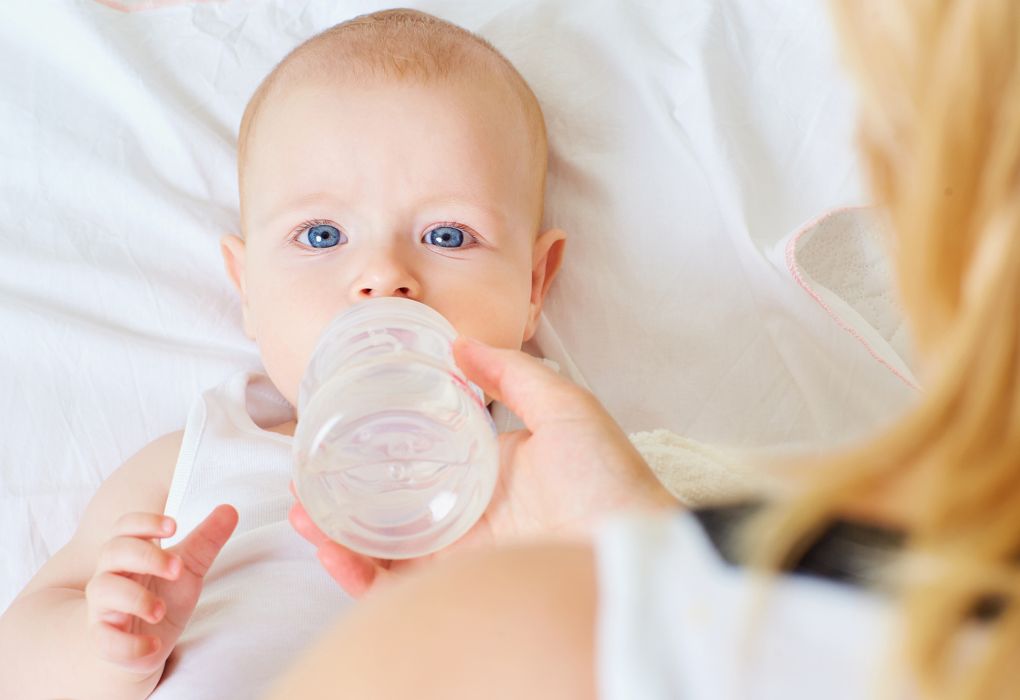 Ein Baby mit einer Milchflasche im Mund schaut in die Kamera.