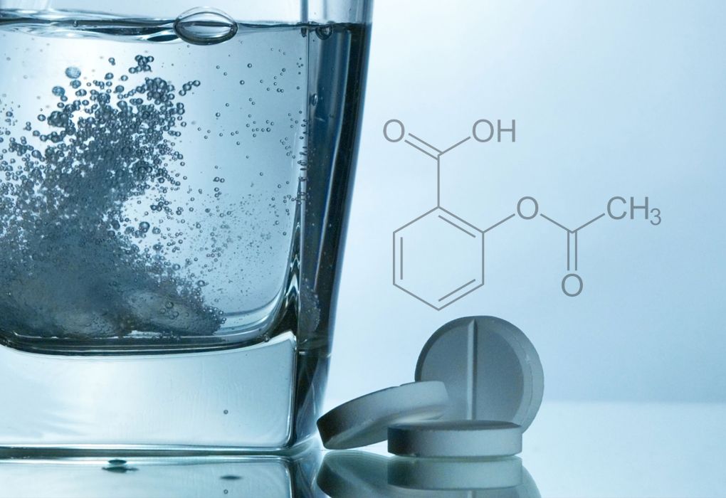 Brausetablette löst sich sprudelnd in einem Glas Wasser auf, daneben chemische Formel