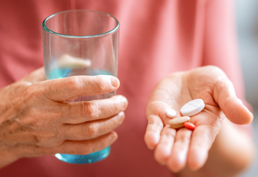 Ältere Person hält eine Tablette in der einen Hand und ein Glas Wasser in der anderen Hand