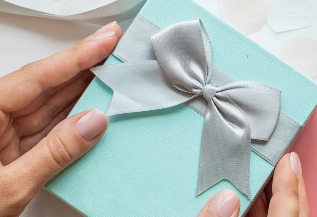 Hände halten ein türkisfarbenes Geschenk mit silberner Schleife