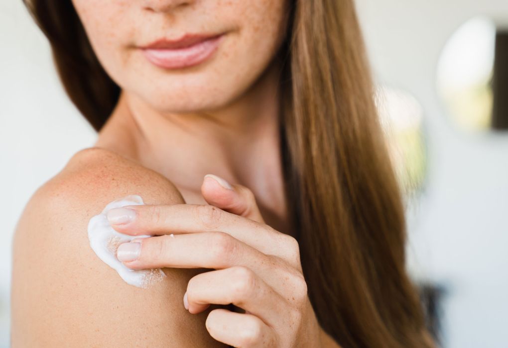 Frau trägt weiße Creme auf ihre Schulter auf