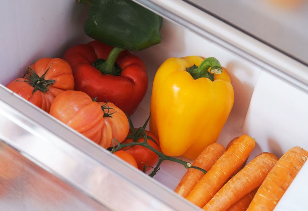 Paprika, Karotten und weiteres Gemüse im geöffneten Kühlschrankfach.