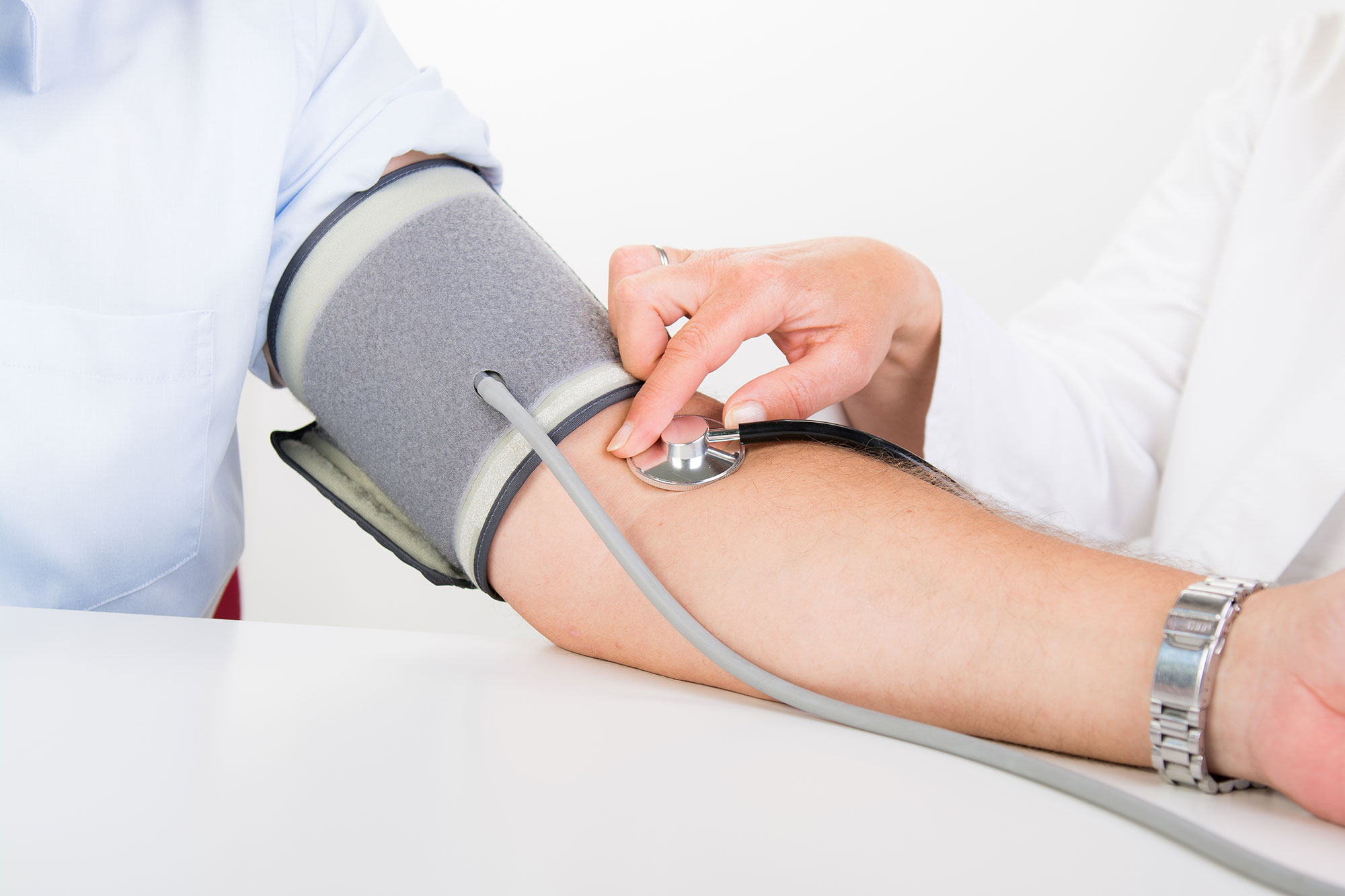 Person misst Blutdruck mit Manschette am Oberarm in einer Praxis