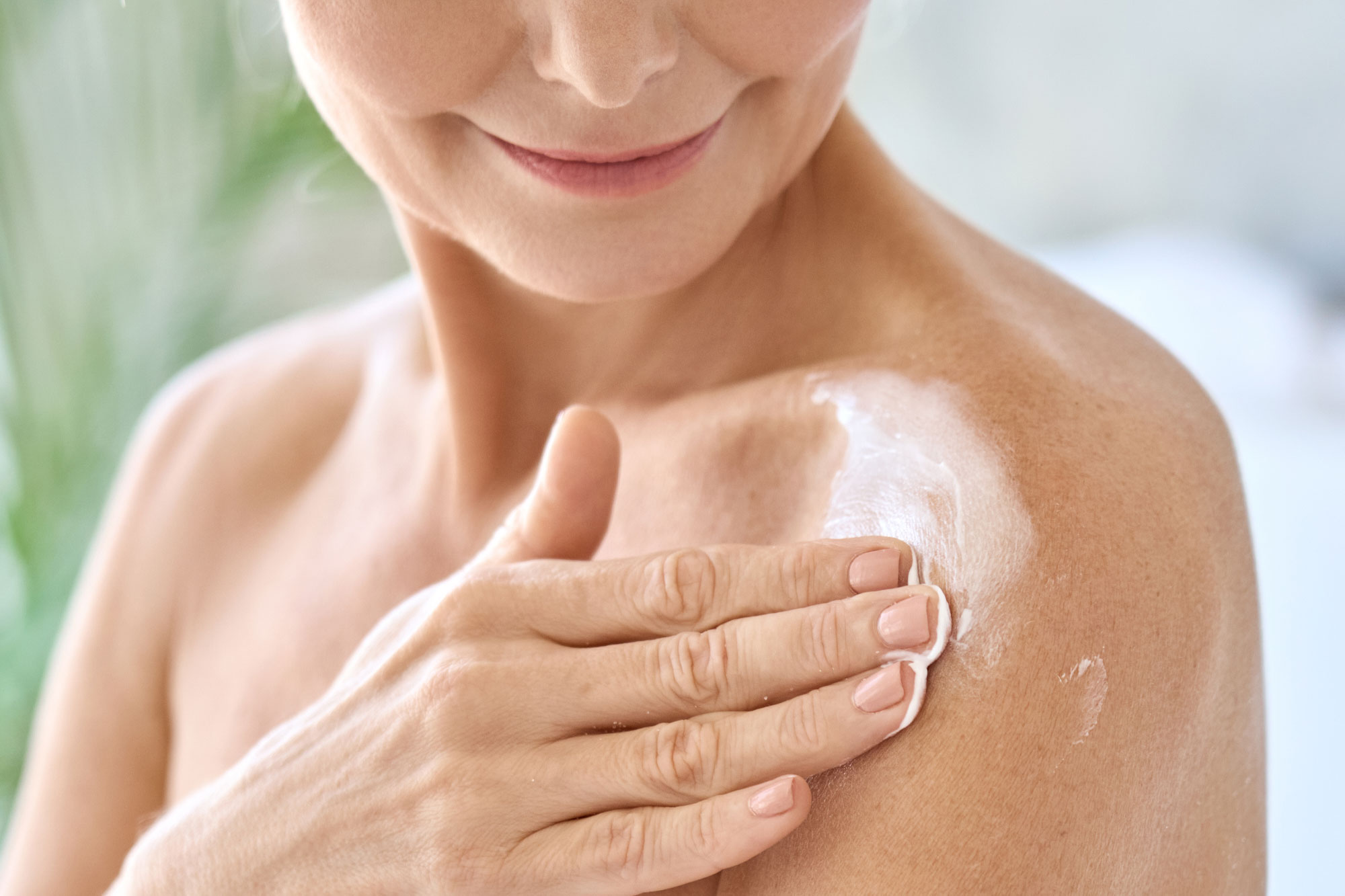 Frau trägt weiße Creme auf ihre Haut auf, um trockene oder gereizte Haut zu pflegen