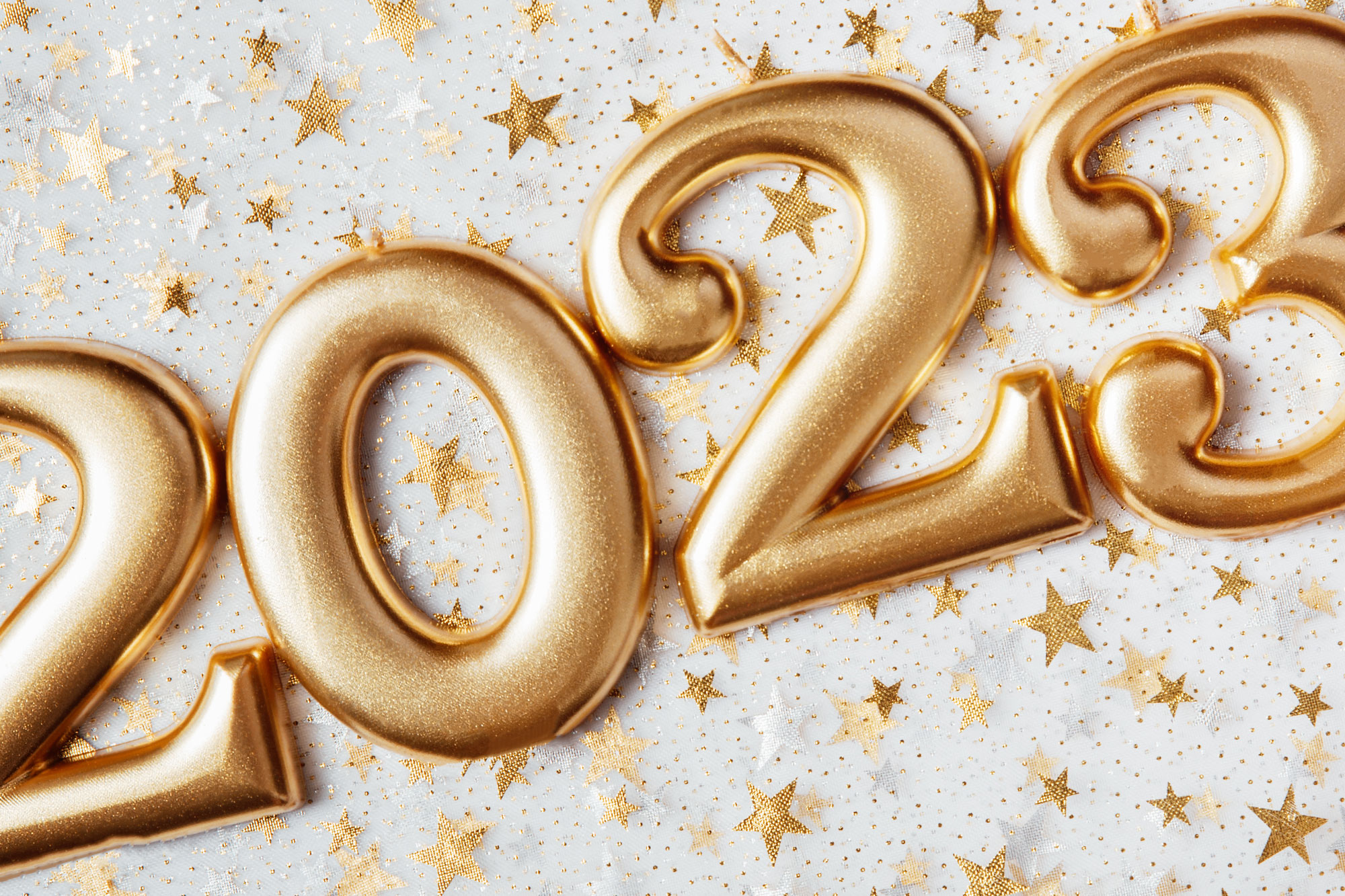 Goldene Luftballons in Form der Zahl 2023 auf hellem Hintergrund mit Sternkonfetti