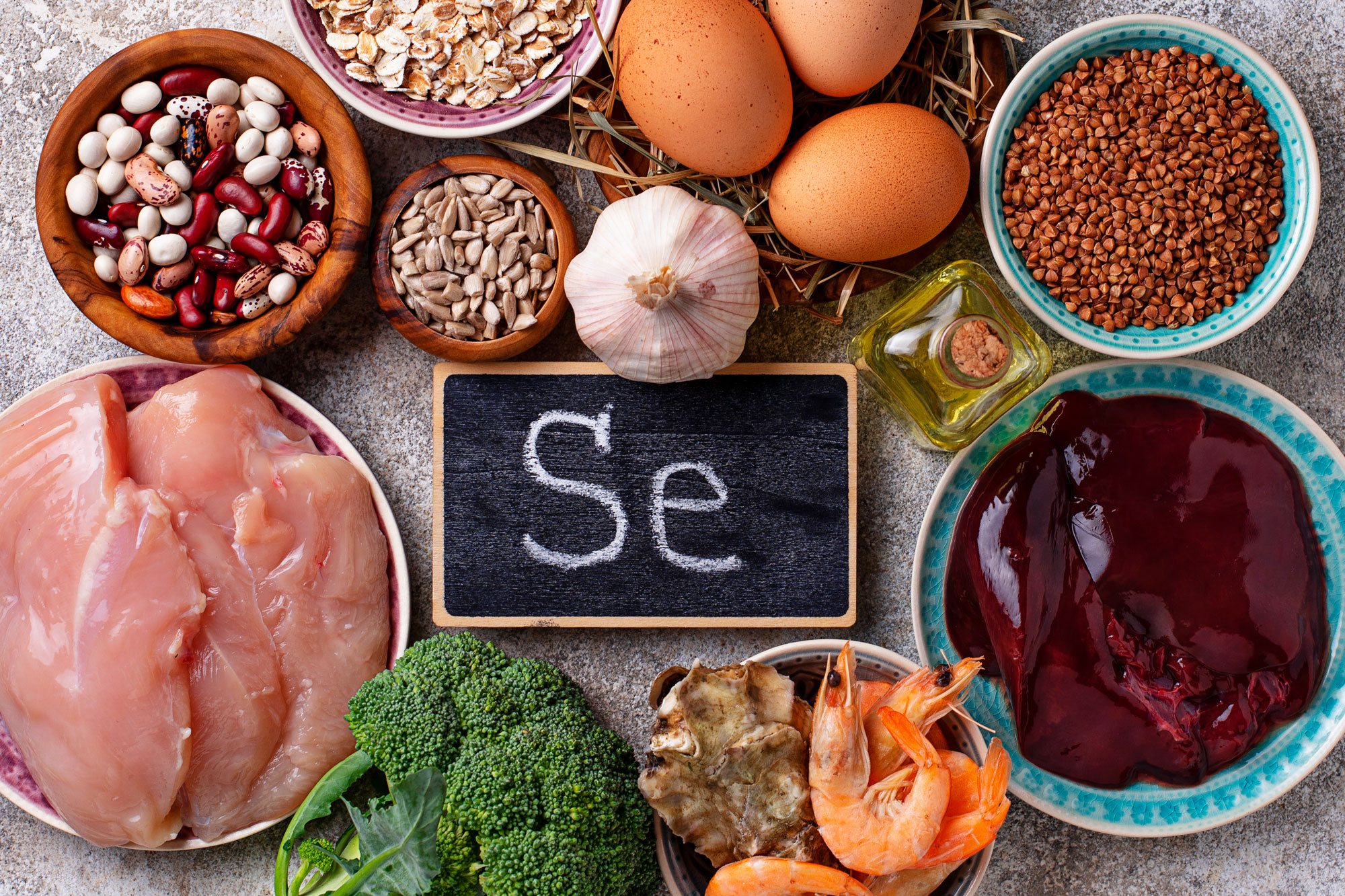 Auswahl an selenreichen Lebensmitteln wie Nüsse, Fisch, Fleisch, Eier und Gemüse mit Kreidetafel „Se“