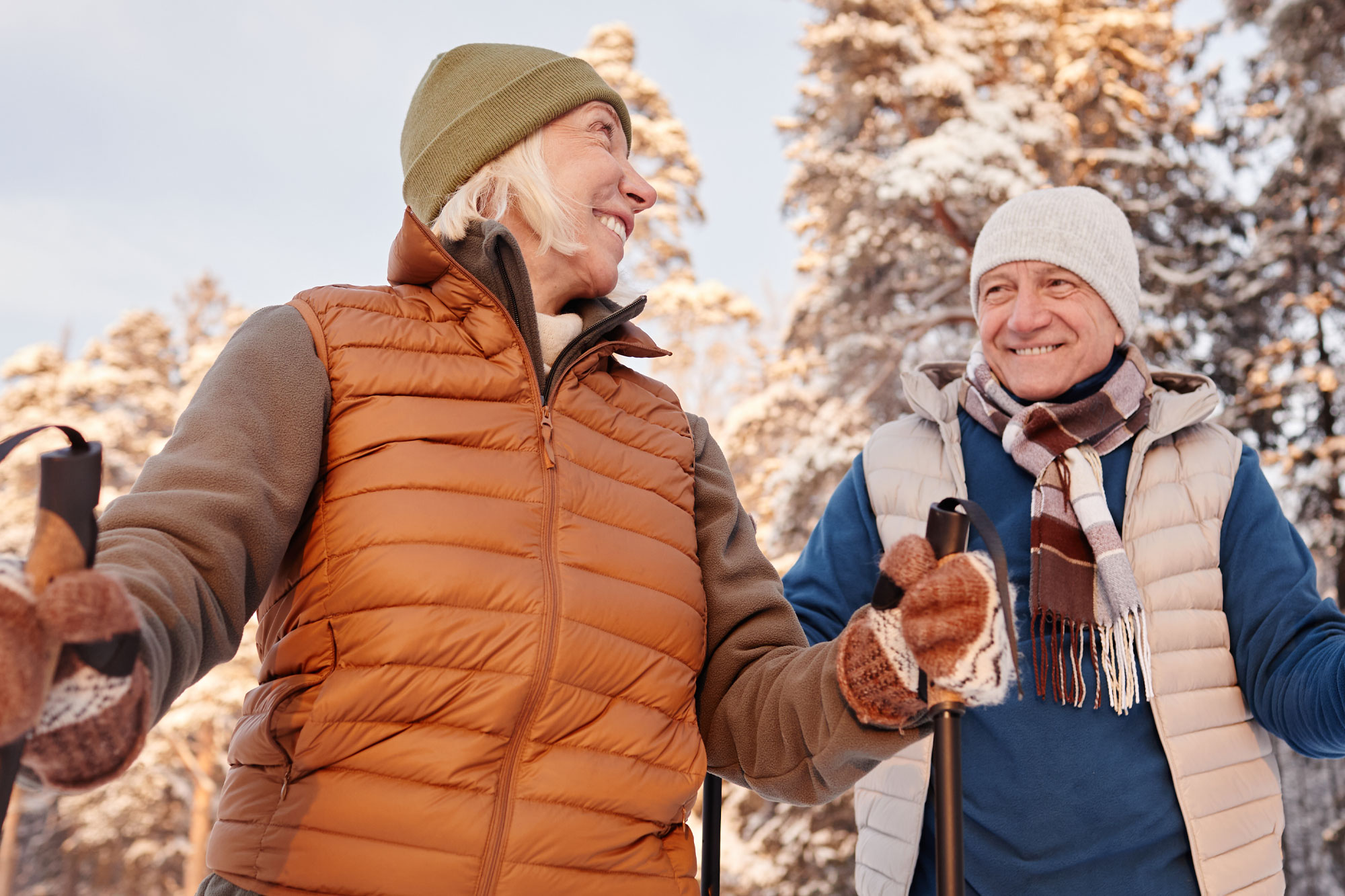 Älteres Paar spaziert lachend im verschneiten Wald und genießt Bewegung an der frischen Luft
