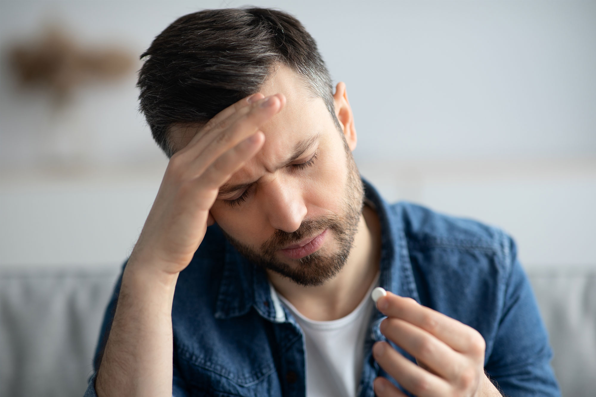 Mann fasst sich an die Schläfe und hält Schmerztablette in der Hand
