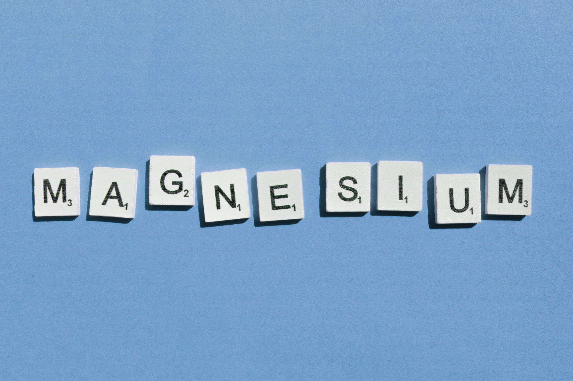 Scrabble-Buchstaben bilden das Wort Magnesium auf blauem Hintergrund