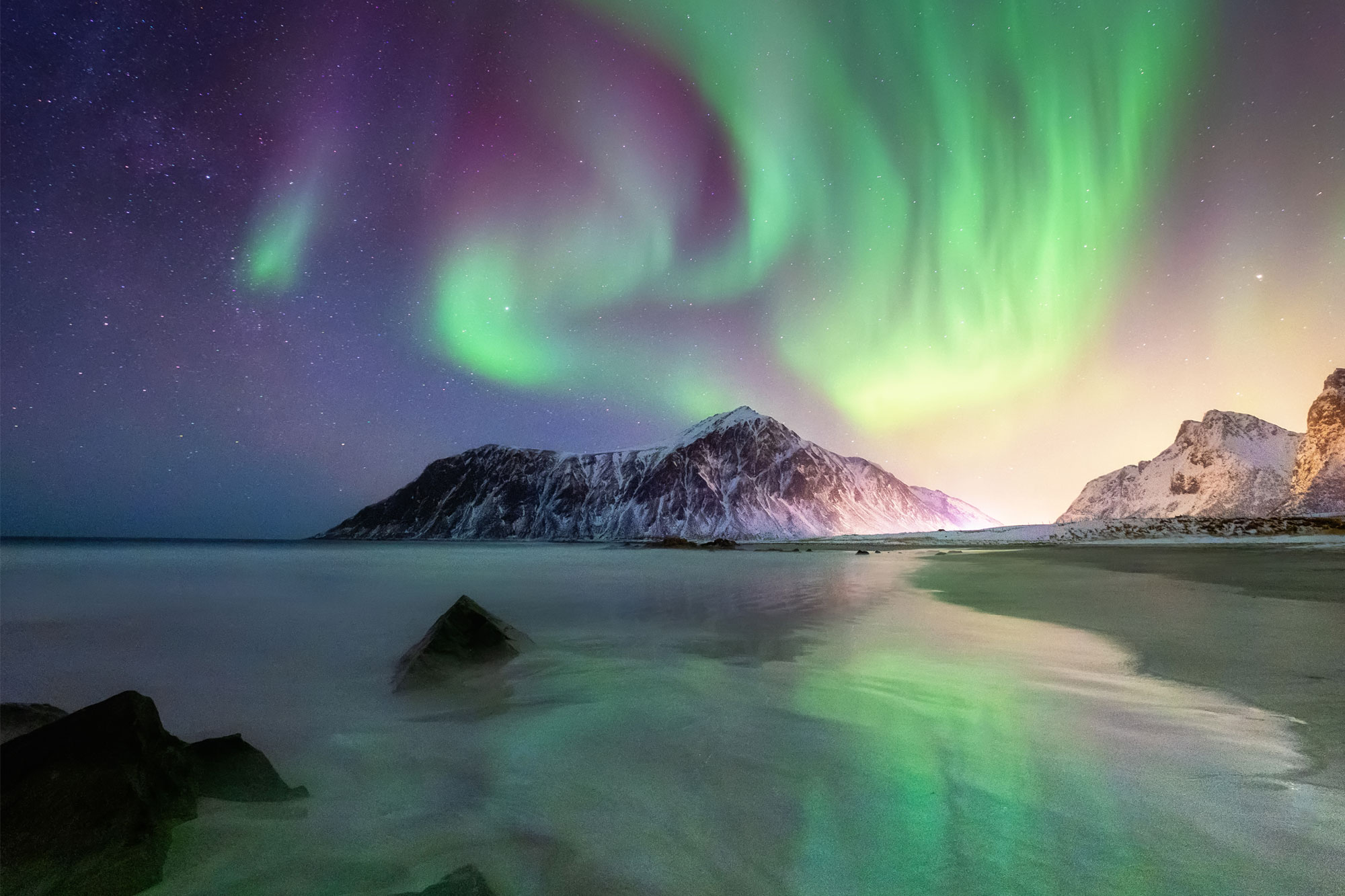 Farbintensive Polarlichter leuchten am Nachthimmel über verschneiten Bergen und Küste