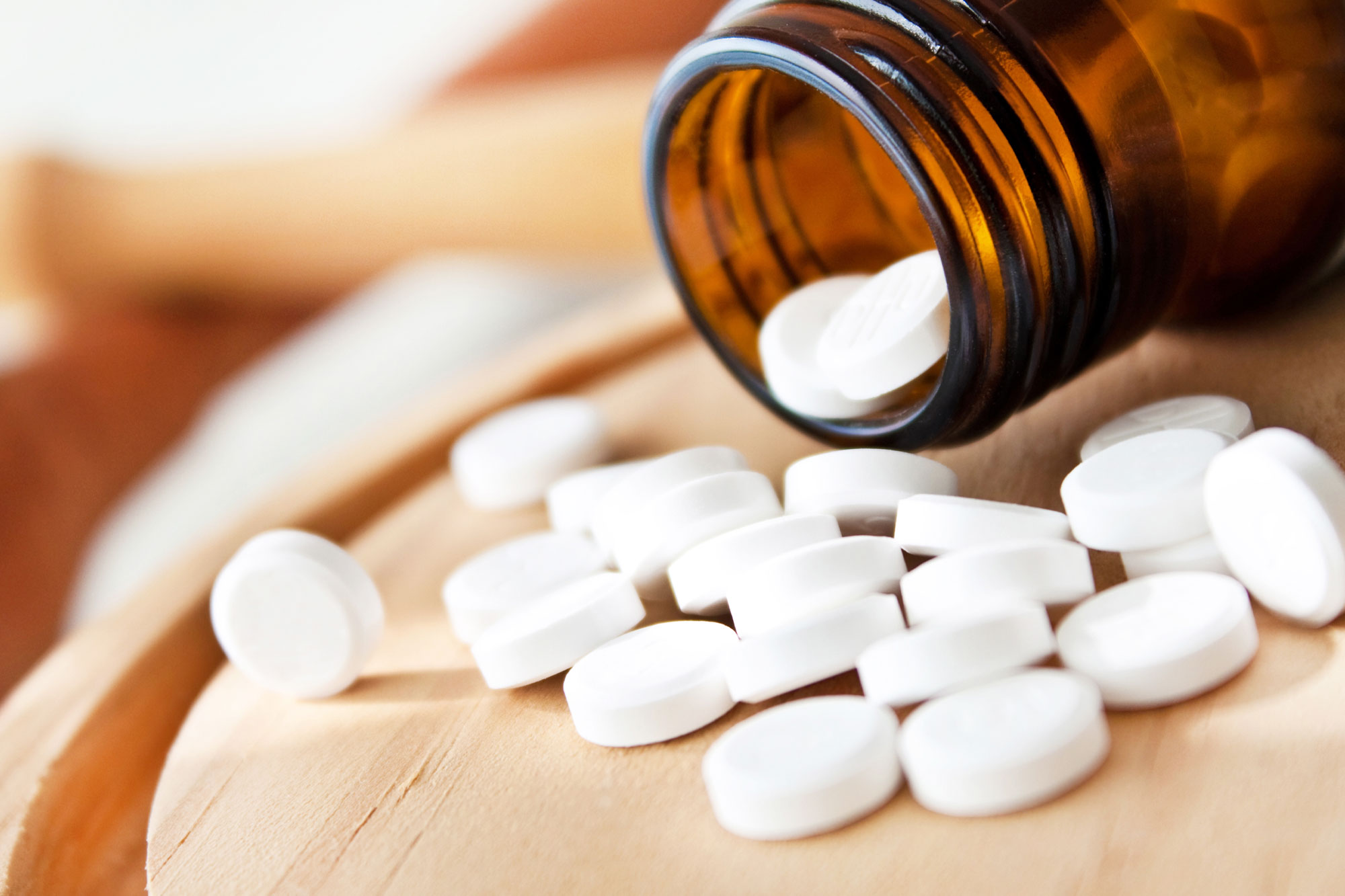 Braune Glasflasche mit weißen Tabletten, Schüßler-Salze auf hellem Holzuntergrund