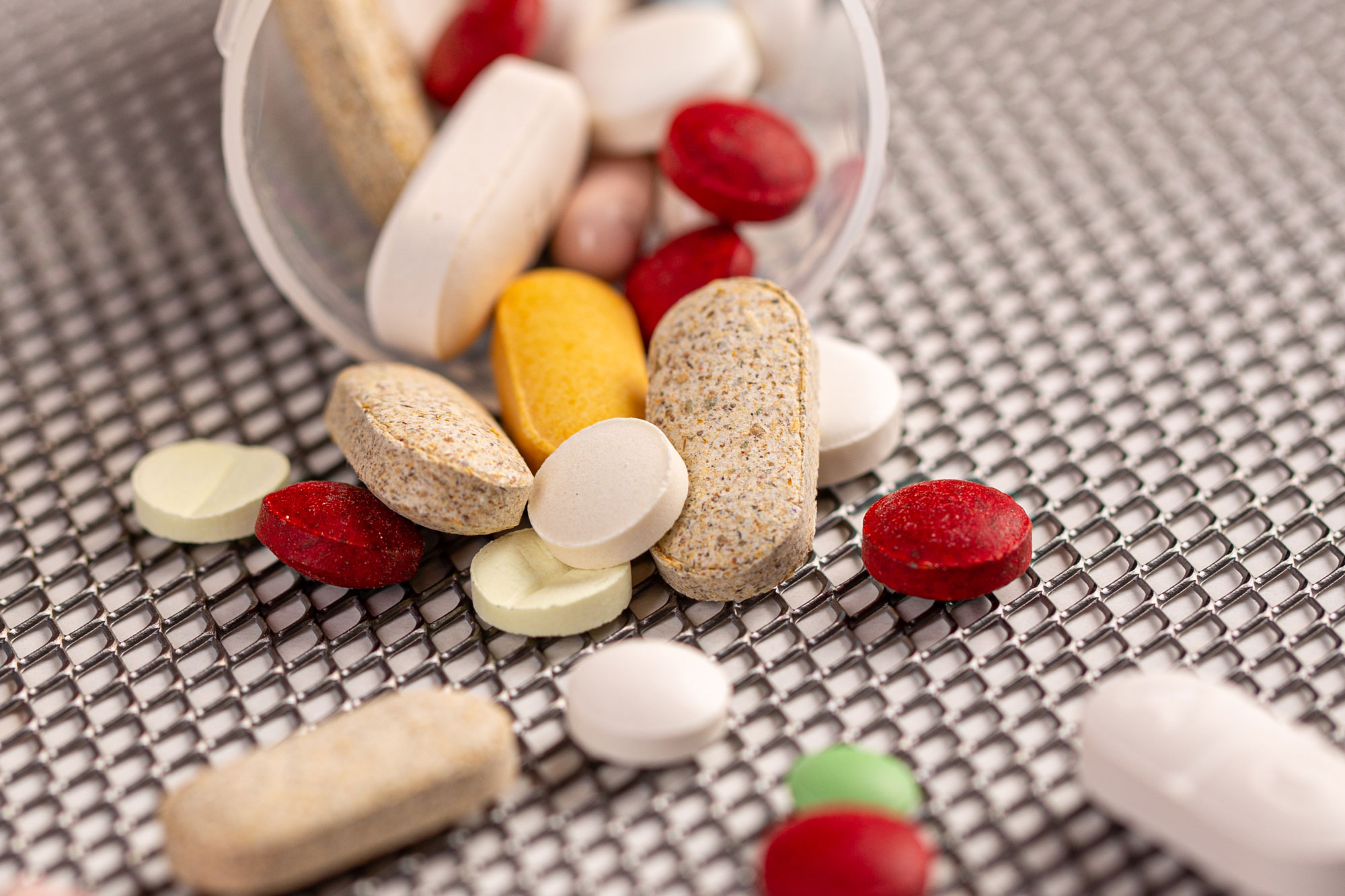 Verschiedene Vitamin-Kapseln und Tabletten in bunten Farben auf grauer Unterlage