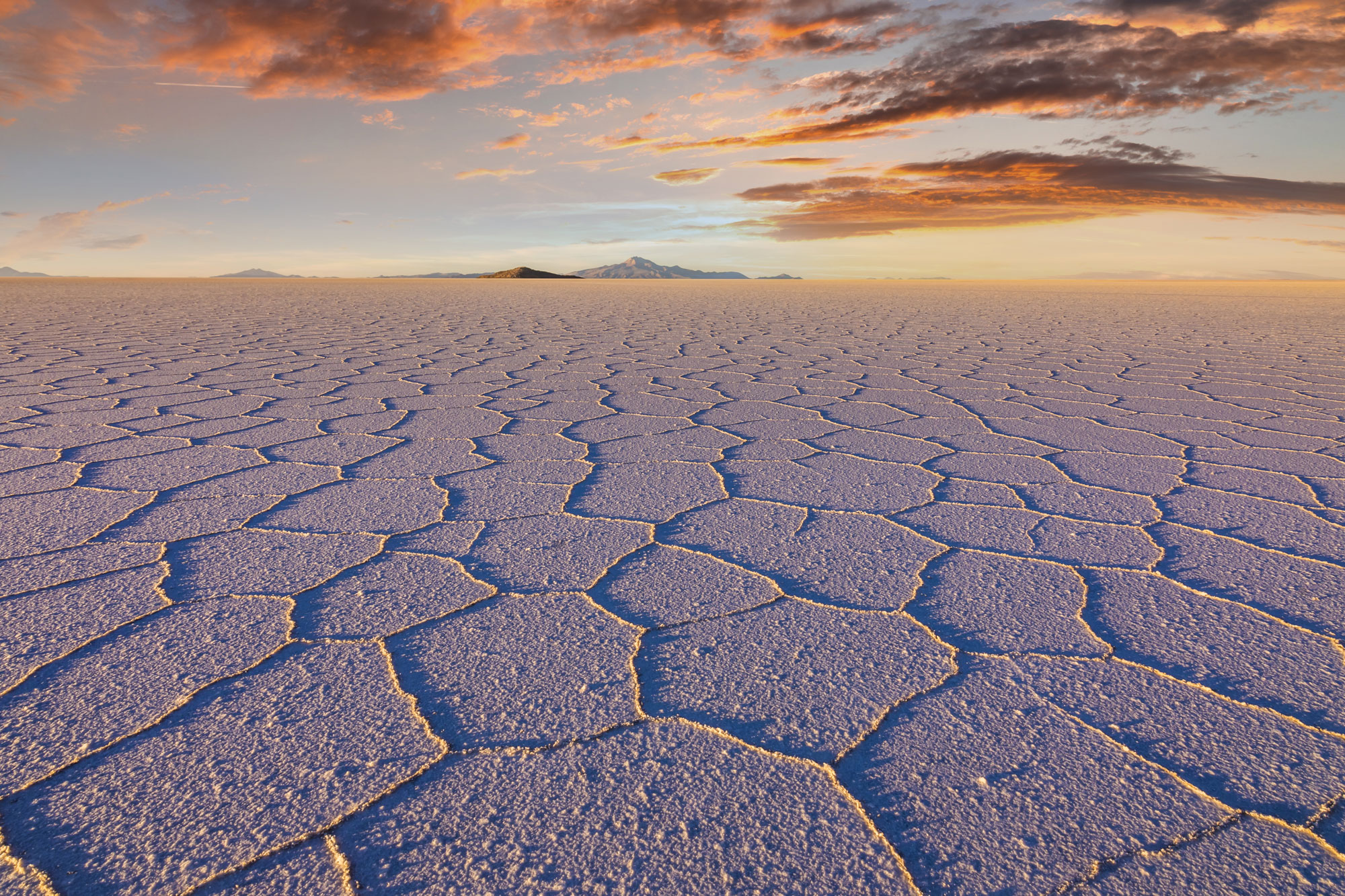 Ausgetrocknete Salzkruste mit polygonalen Mustern in einer weiten Wüstenlandschaft bei Sonnenuntergang