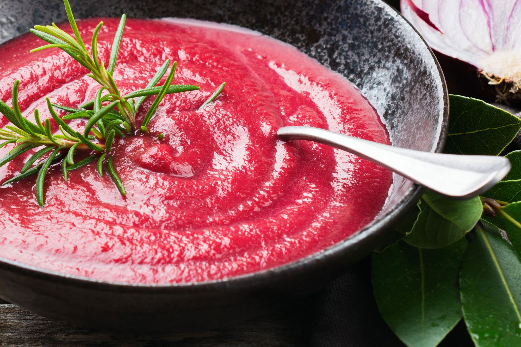 Teller mit roter Cremesuppe, dekoriert mit frischem Rosmarin und Löffel am Rand