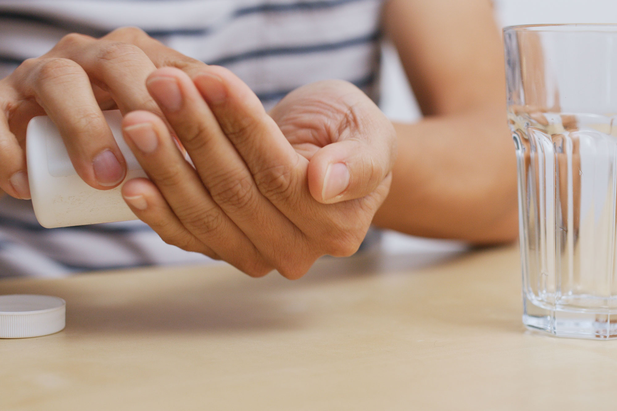 Mann legt eine Tablette in die Hand und hält daneben ein Glas Wasser