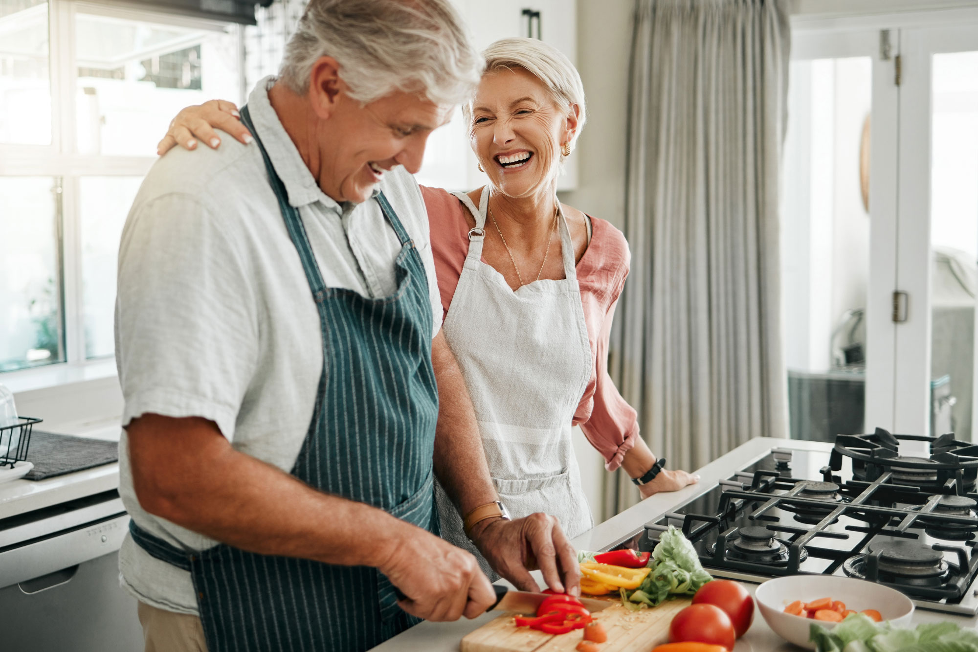Älteres Paar steht in der Küche und bereitet lachend frisches Gemüse zu