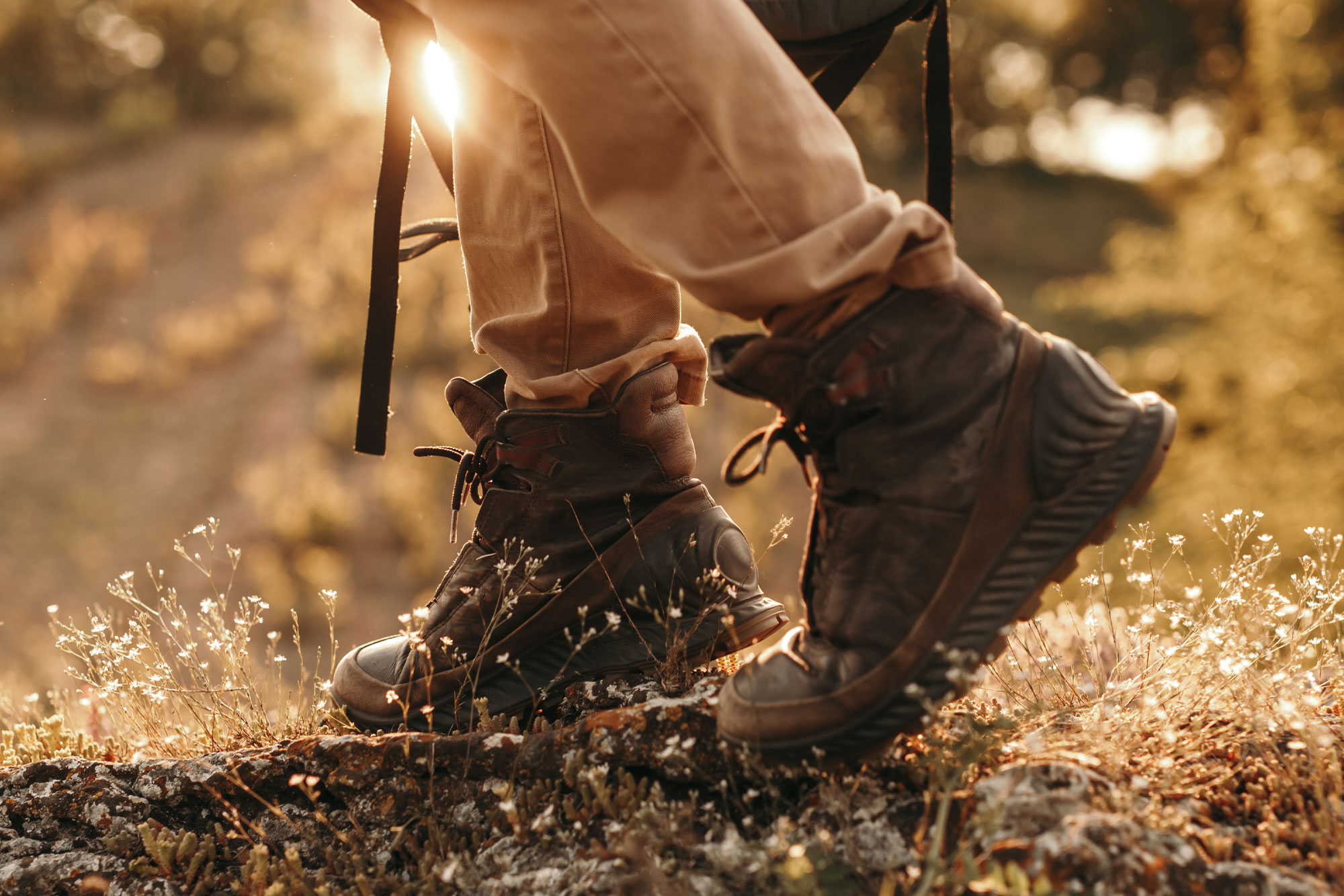Person mit Wanderstiefeln läuft mit Trekkingstöcken über einen sonnigen Waldweg