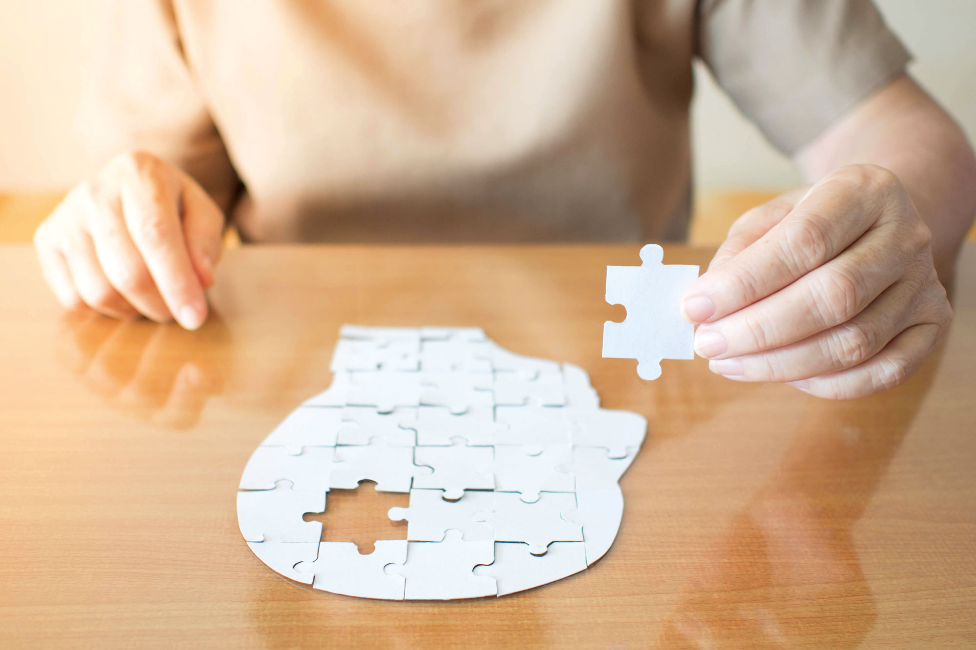 Person setzt ein weißes Puzzle in Form eines menschlichen Kopfes zusammen