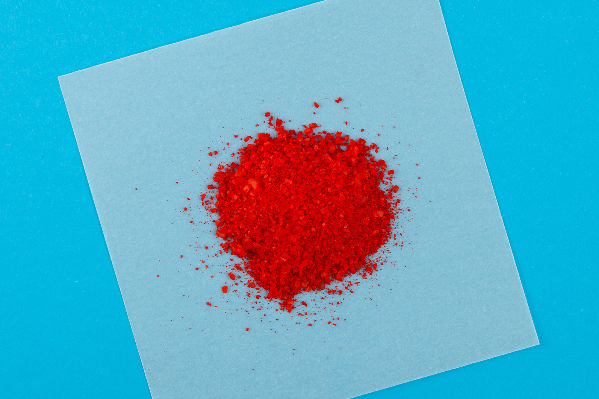 Heller Haufen roten Pulvers auf quadratischem weißen Papier vor blauem Hintergrund