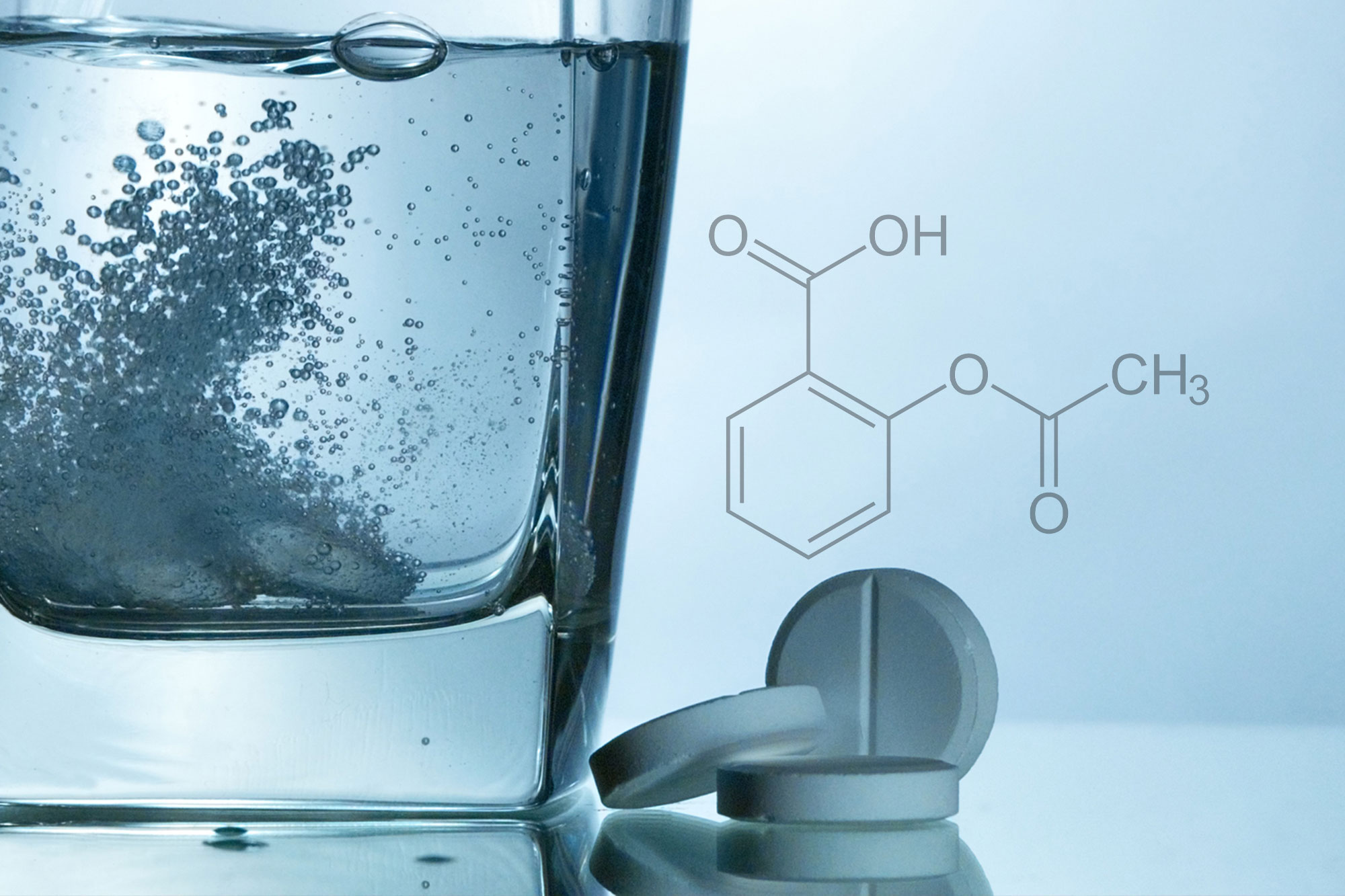 Brausetablette löst sich sprudelnd in einem Glas Wasser auf, daneben chemische Formel
