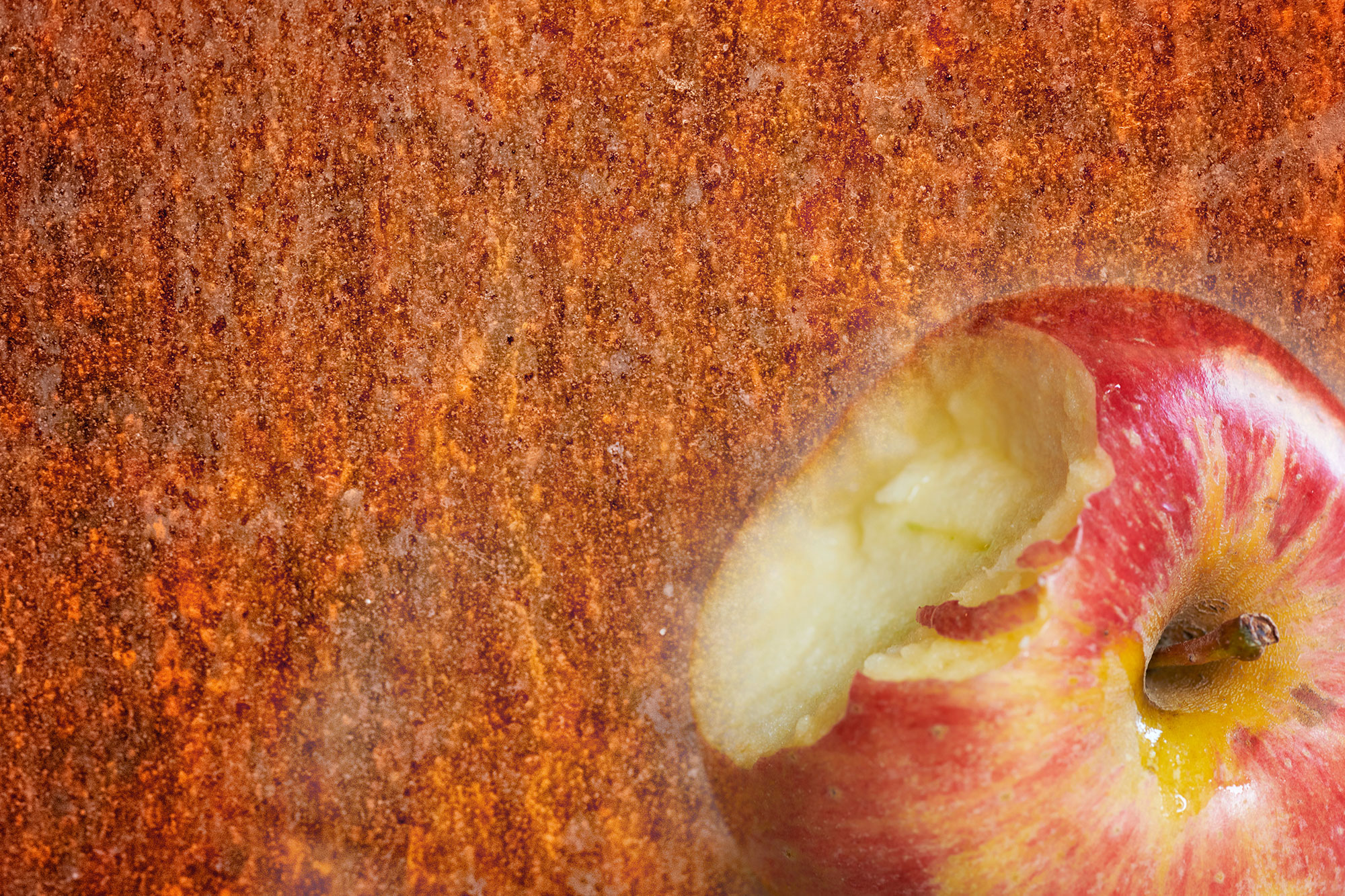 Rostige Metalloberfläche im Hintergrund, im Vordergrund ein angebissener Apfel