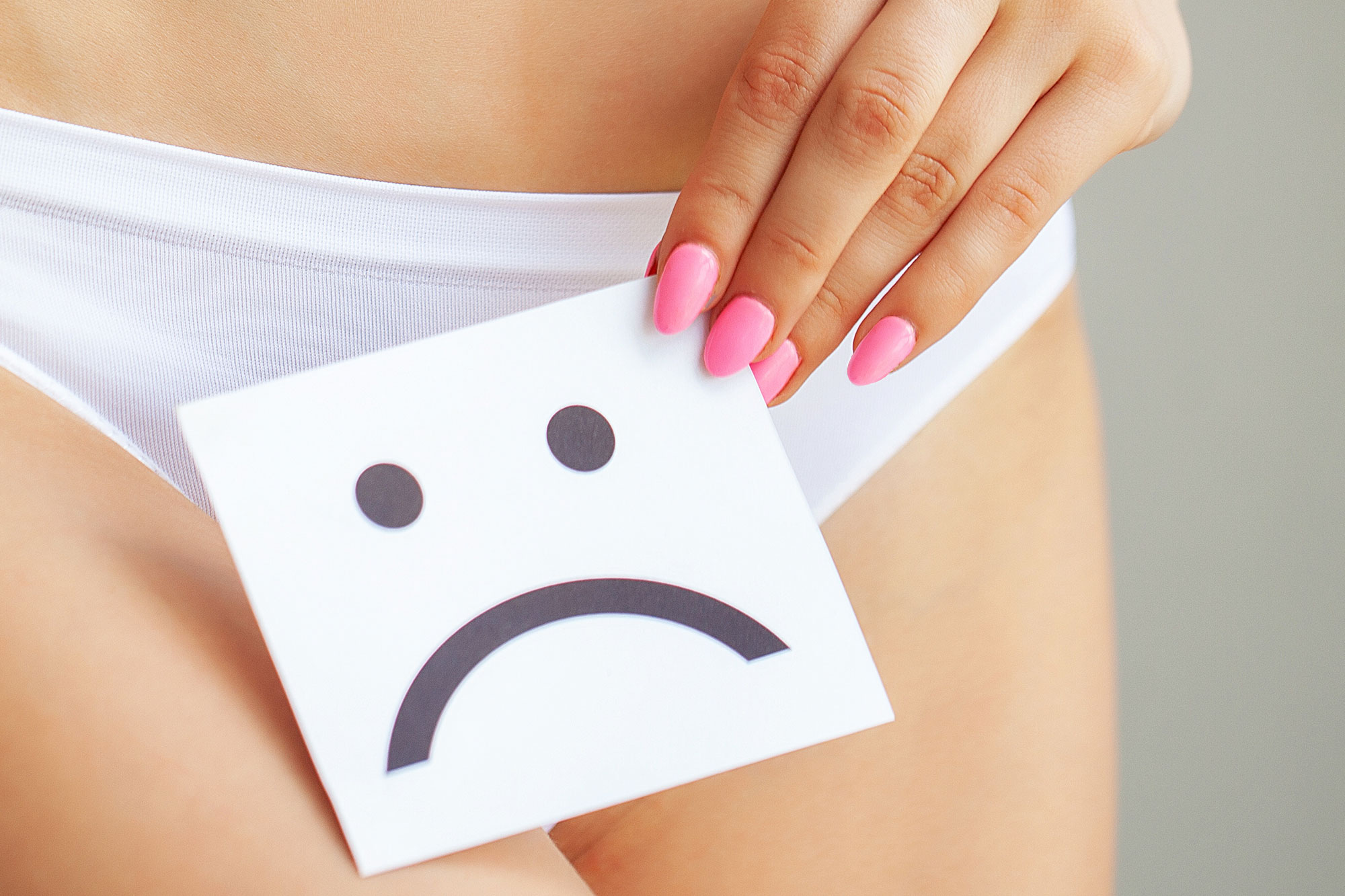 Frau hält ein Blatt Papier mit traurigem Smiley vor den Slip