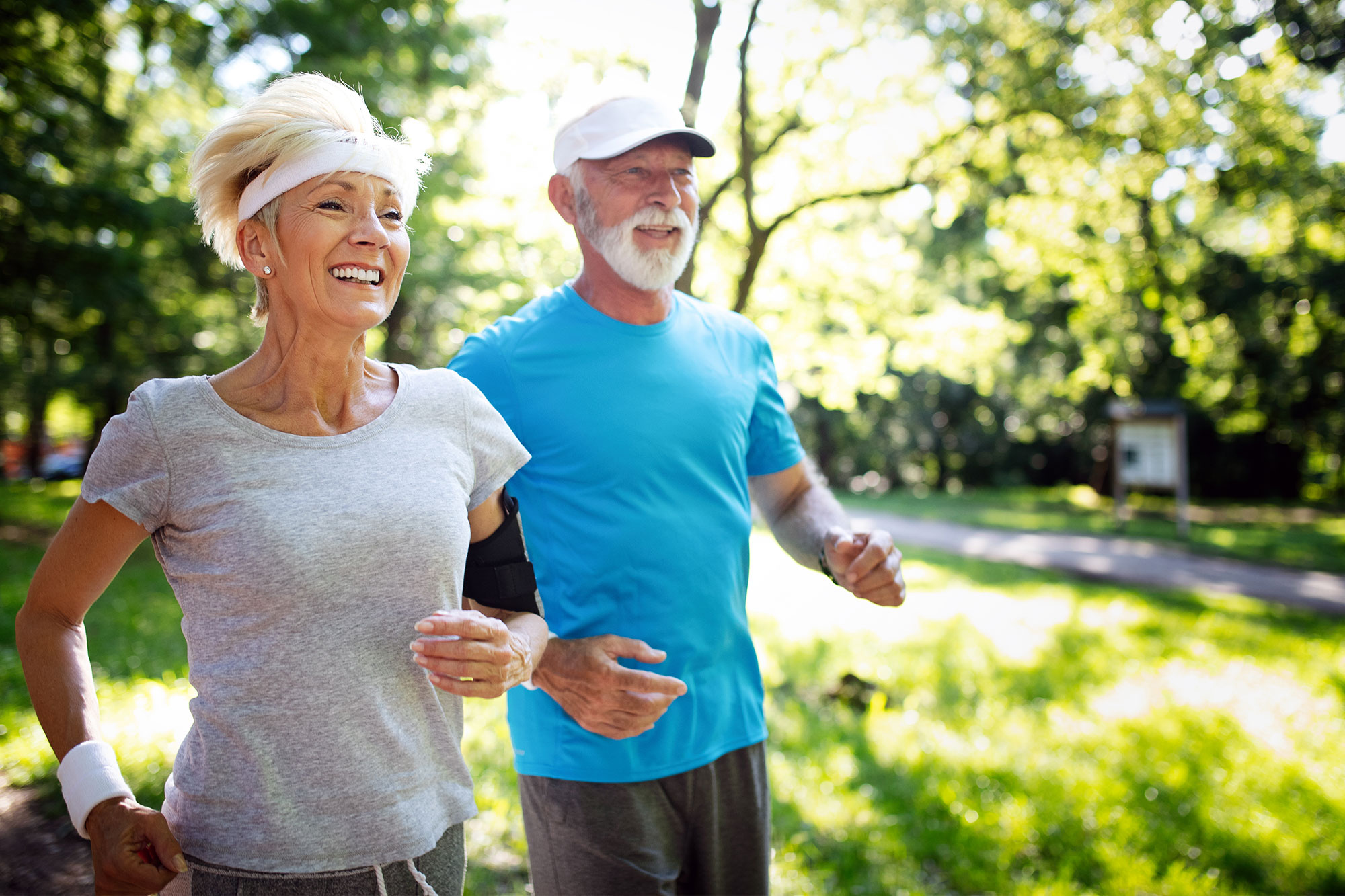 Älteres Paar joggt lachend bei Sonnenschein im Park
