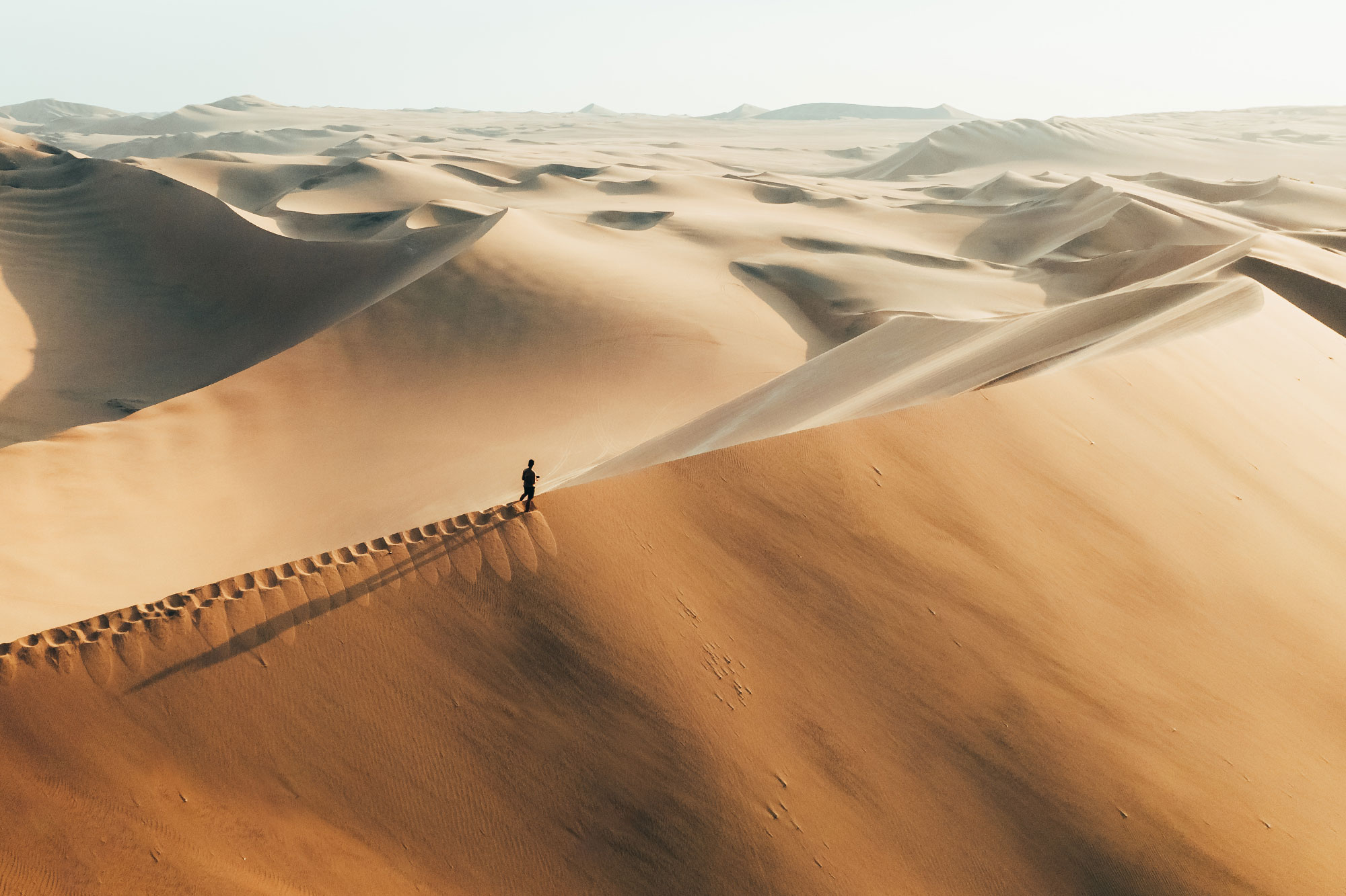 Goldfarbene Sanddünen mit winziger Menschenspur in weiter Wüstenlandschaft