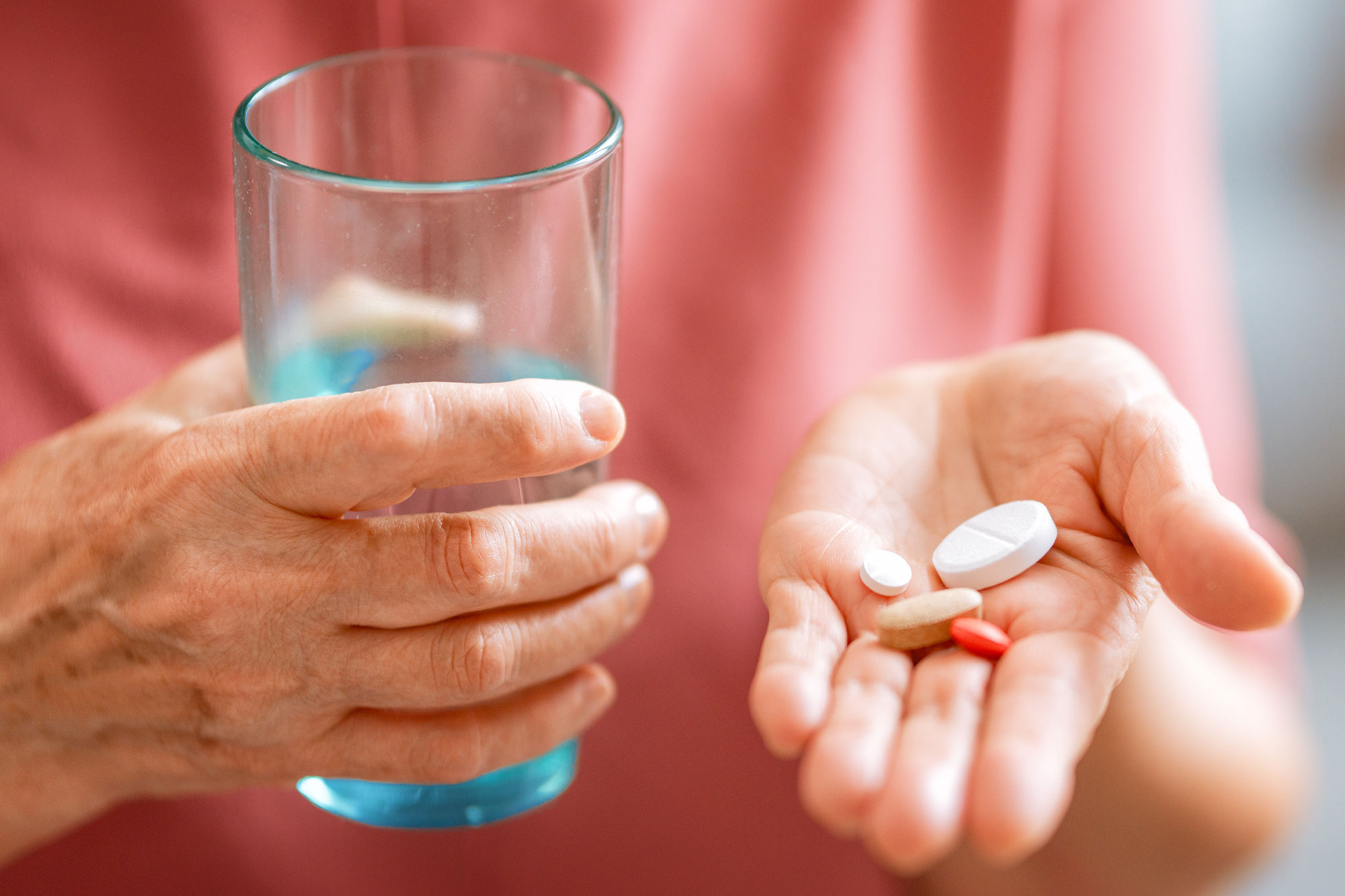 Ältere Person hält eine Tablette in der einen Hand und ein Glas Wasser in der anderen Hand