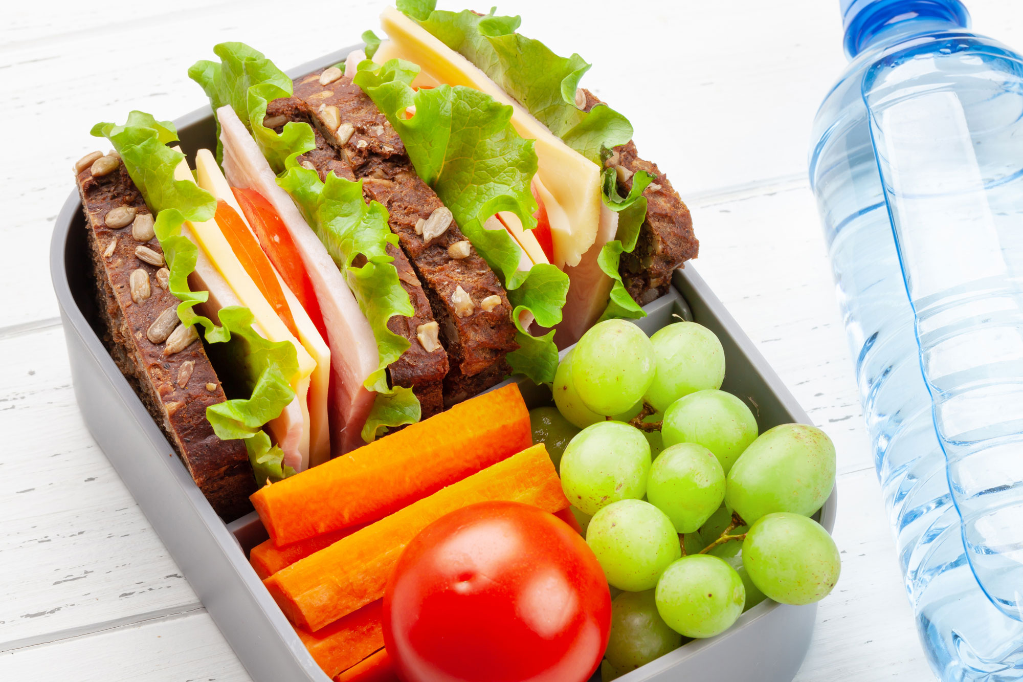 Brotdose gefüllt mit Sandwich, Tomaten, Weintrauben und Wasserflasche