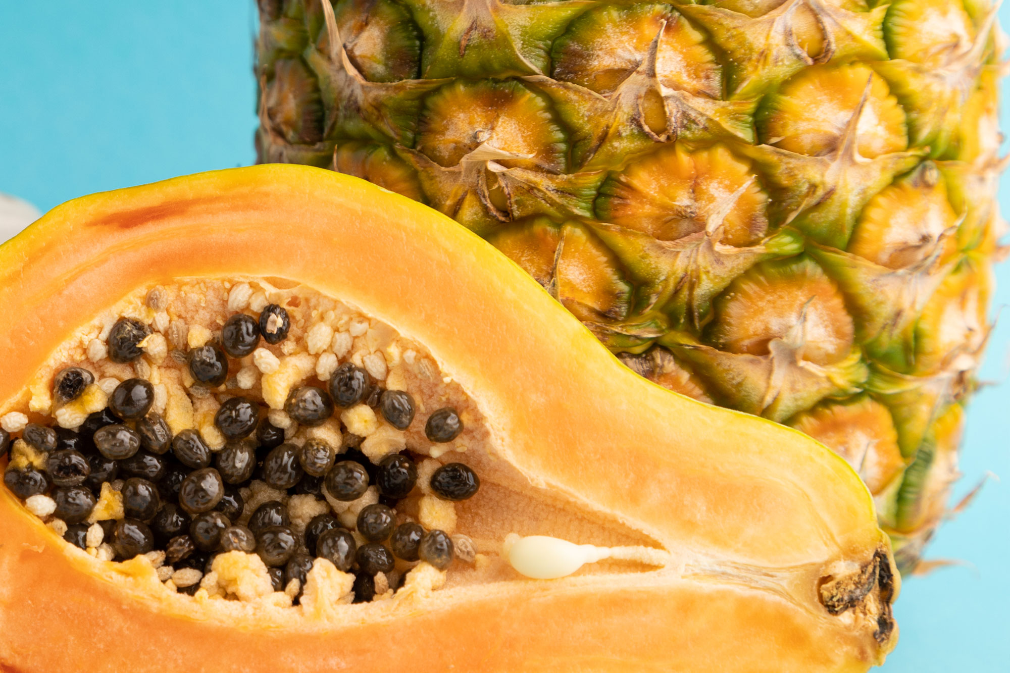 Aufgeschnittene Papaya mit Kernen und eine Ananas nebeneinander