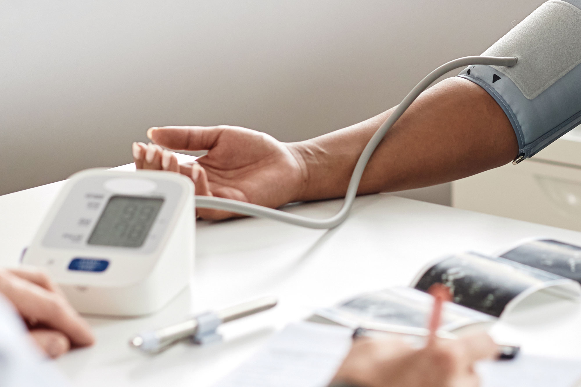 Person misst den Blutdruck mit elektronischem Messgerät am Arm in einer Praxis