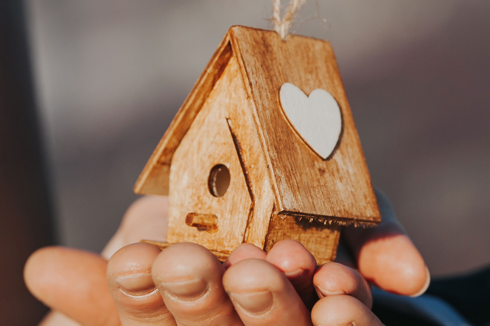 Hände halten ein kleines Holzhaus mit ausgestanztem Herz in der Mitte