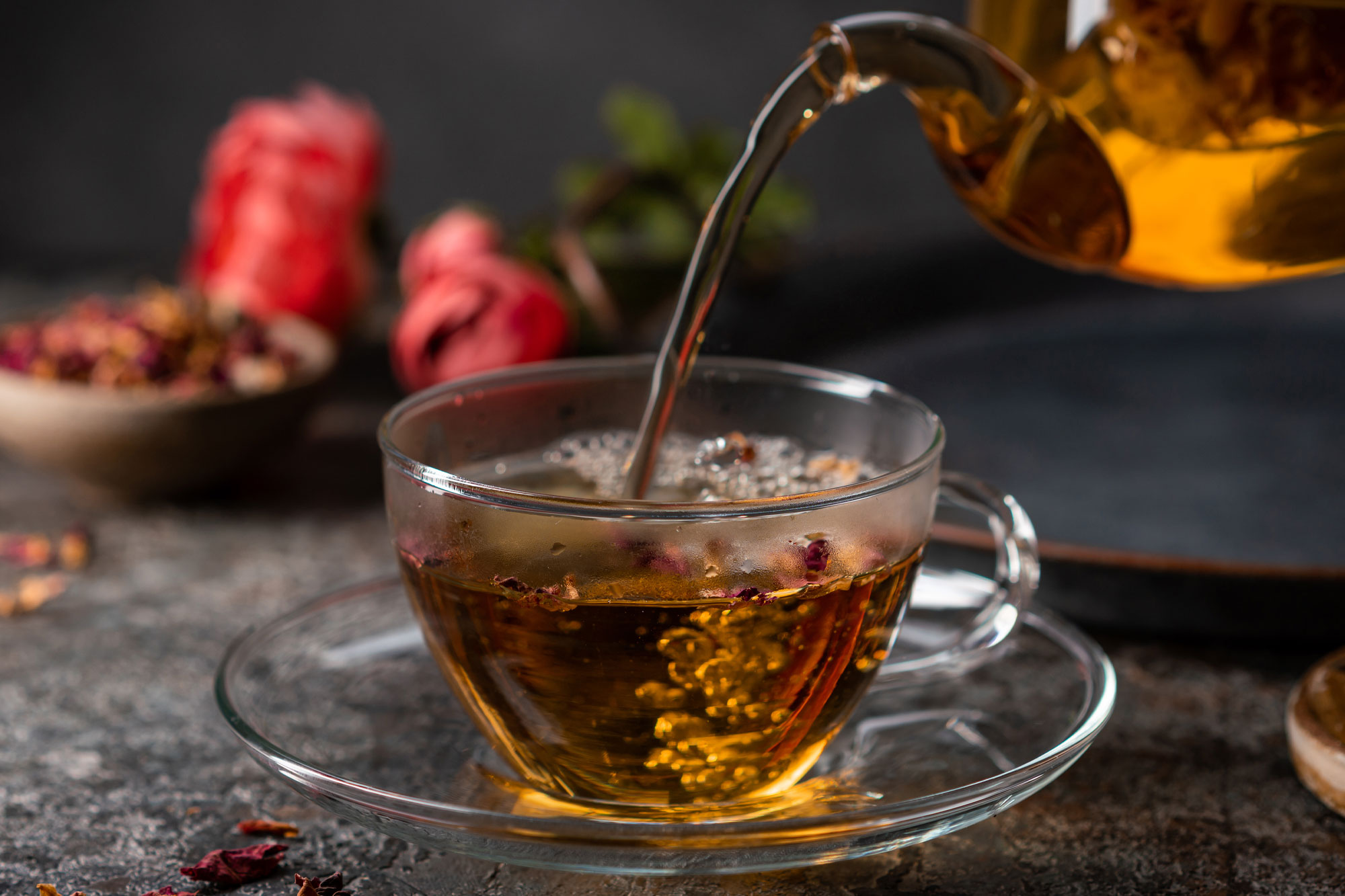 Frisch aufgegossener Tee wird aus einer Kanne in ein Glas eingeschenkt, dekoriert mit winterlichen Gewürzen